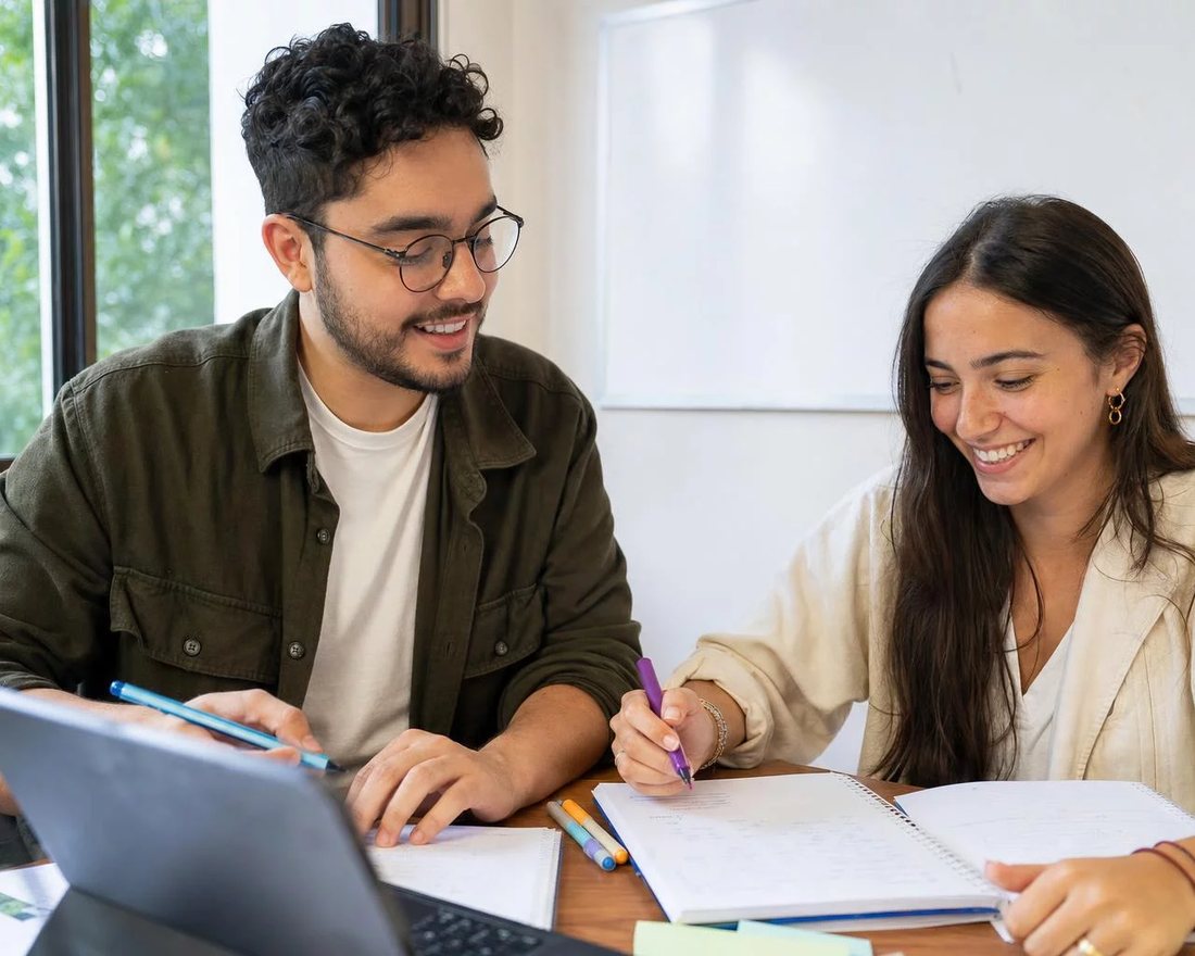 Reunião de trabalho em volta de uma mesa com laptop, papéis e xícaras, alguém defendendo uma proposta